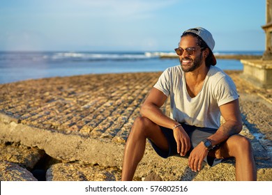 Relaxed and cheerful. Outdoor portrait of happy young african man sitting near the sea.