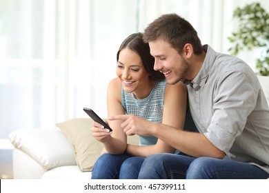 Relaxed couple or friends using a generic mobile phone together sitting on a sofa in the living room at home - Powered by Shutterstock