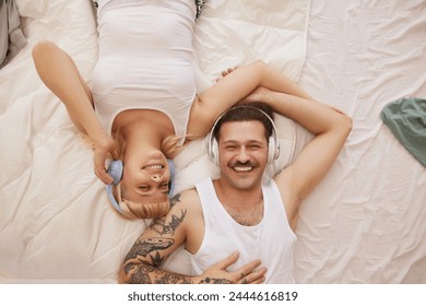 Relaxed couple with headphones listening to music in bed - Powered by Shutterstock