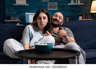 Relaxed couple sitting on couch watching movie on television, drinking beer playing popcorn games enjoying time together at home leisure, happiness and married people concept.