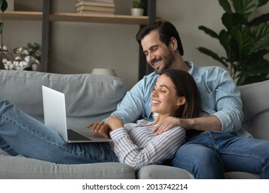 Relaxed couple spend weekend at home use laptop, spouses rest on comfy sofa look at pc screen, doing online shopping together, enjoy app, buy ticket for leisure, e-commerce happy client family concept Foto Stock