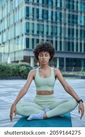 Relaxed Dark Skinned Young Woman Practices Yoga In City Meditates And Breathes Deeply For Stress Relief Poses In Lotus Pose On Rubber Mat Wears Sportsclothes Improves Inner Balance Serene State