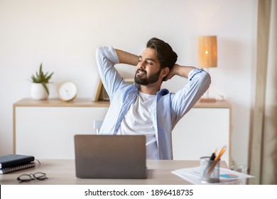 Relaxed Eastern Man Leaning Back In Chair, Resting After Online Work With Laptop, Millennial Arab Guy Sitting At Table With Computer In Home Office With Hands Behind Head And Looking Aside, Free Space