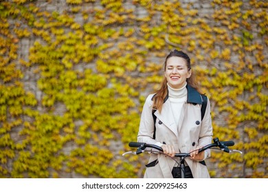 Relaxed Elegant Female In Beige Trench Coat With Bicycle Against The Green Wall Outside In The City.