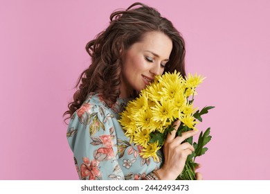 relaxed elegant woman in floral dress with yellow chrysanthemums flowers isolated on pink background.