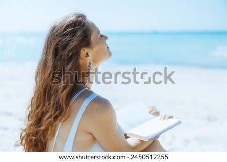 relaxed elegant woman on the seacoast with straw bag and book.