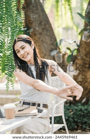 Relaxed female freelancer stretching arms while taking a break from work on her laptop in a lush garden cafe setting.