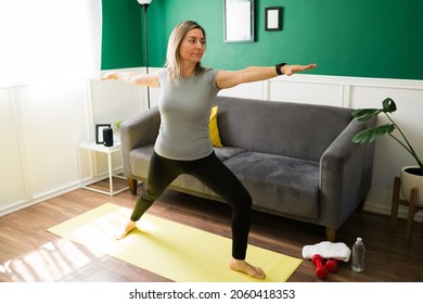 Relaxed And Fit Elder Woman Exercising With Yoga At Home And Doing A Warrior Pose 