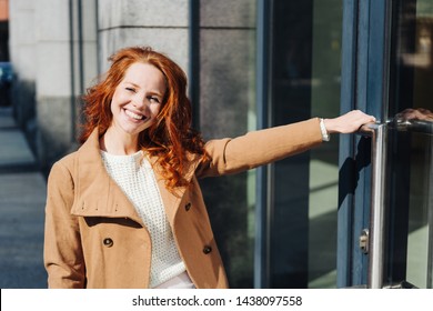 Relaxed Friendly Woman About To Enter A Commercial Building Holding The Handle Of A Large Glass Door With A Happy Smile