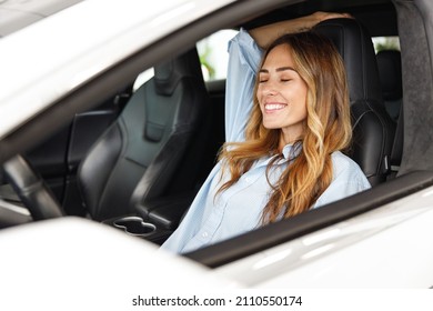 Relaxed fun happy driver woman customer buyer client in blue shirt close eyes sit in car choose auto want buy new automobile in showroom vehicle salon dealership store motor show indoor.Sales concept