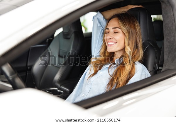 Relaxed fun happy driver woman customer buyer\
client in blue shirt close eyes sit in car choose auto want buy new\
automobile in showroom vehicle salon dealership store motor show\
indoor.Sales concept