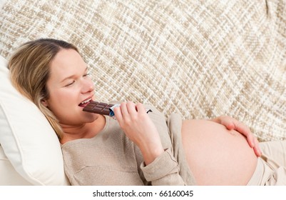 Relaxed Future Mom Eating A Chocolate Bar Lying On The Sofa At Home