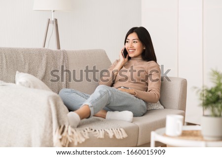 Relaxed girl chatting on phone, smiling and listening to call, sitting on sofa, free space