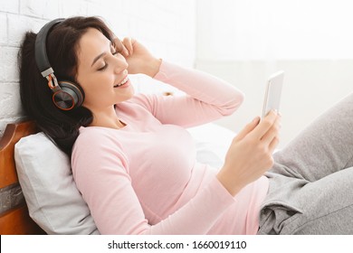 Relaxed girl listening to music with wireless headphones and smartphone in bed, empty space - Shutterstock ID 1660019110