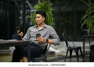 Relaxed and handsome millennial Asian man using his smartphone and sipping coffee at a coffee shop outdoor space. - Powered by Shutterstock