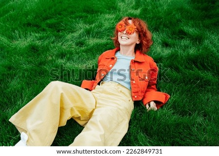 Relaxed Happy smiling redhead Woman with freckles and red orange gerbera Flower sunglasses lying on green grass and enjoy the moment. Positive vibe Emotions. Fashion girl. Spring, summer mood.