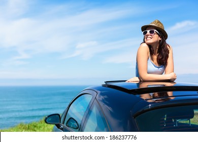 Relaxed Happy Woman On Summer Travel Vacation To The Coast  Leaning Out Car Sunroof With The Sea On Background.