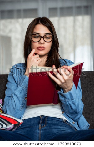 Relaxed happy woman reading a book  sitting on a couch at home
