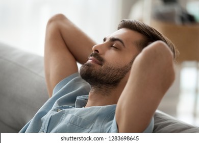 Relaxed happy young man resting having nap on comfortable couch breathing fresh air, lazy tired guy stretching enjoying stress free peaceful day feeling lounge mood at home, peace of mind concept