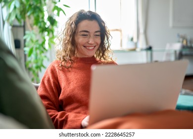 Relaxed happy young woman sitting on sofa using laptop at home surfing, doing online ecommerce shopping, looking at computer ordering sale products on website, watching videos or elearning. - Powered by Shutterstock