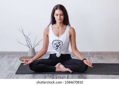 Relaxed Harmonious Beautiful Brunette Woman Yoga Instructor Doing A Lotus Position With Closed Eyes While Sitting On A Rug On Floor During A Workout. Health And Spirit Improvement Concept. Copyspace