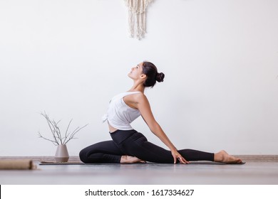 Relaxed Harmonious Beautiful Brunette Woman Yoga Instructor Doing One Legged King Pigeon Pose, Sitting On Mat On Wooden Floor At Workout In White Yogi Classroom. Health And Spirit Improvement Concept