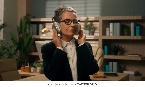 Relaxed having fun work pause freedom Caucasian senior business woman middle-aged businesswoman adult mature female employer in office listening music in wireless headphones enjoy audio song dancing