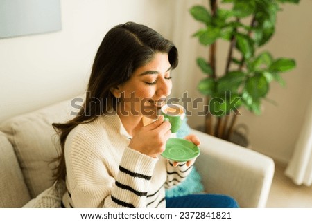 Relaxed hispanic young woman smiling drinking espresso coffee while relaxing at home during a cozy morning