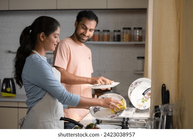 Relaxed indian couples washing dishes together at kitchen during weekend - concept of sharing housework, spending time together and relationship caring - Powered by Shutterstock