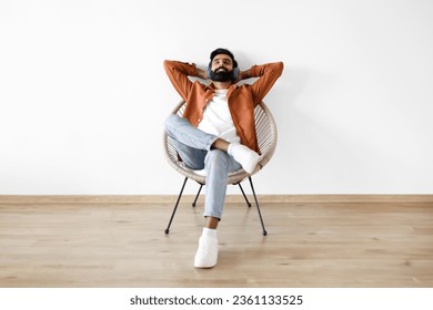 Relaxed Indian Young Man With Wireless Headphones Resting And Listening To Music On Weekend, Sitting In Chair With Hands Behind Head, Enjoying Break And Relaxation Time At Home - Powered by Shutterstock