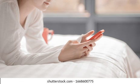 Entspannte kleine Frau mit einem Smartphone am Morgen auf dem Bett zu Hause