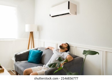 Relaxed man chilling and resting on the sofa while enjoying the new ac unit during a hot summer - Shutterstock ID 2146836777