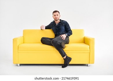 Relaxed man with coffee mug in hands sitting on comfort bright sofa looking to camera. good morning concept - Shutterstock ID 2174619391
