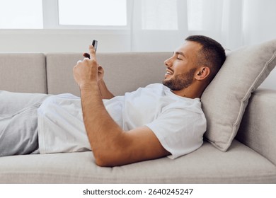Relaxed man engaging with technology while lounging on a couch, reflecting themes of digital detox and work-life blur. A candid moment of solitude and self-care.