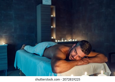 A relaxed man enjoys moments after massage in the spa center. All around are fragrant candles. Aromatherapy and massage. A man at massage in spa center.