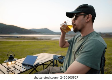 A relaxed man enjoys a peaceful moment sipping tea by a serene lakeside as the evening sets in.

 - Powered by Shutterstock