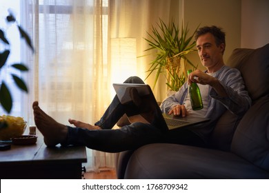 Relaxed Man Entertaining With A Laptop At Home Having A Beer Sitting On A Sofa