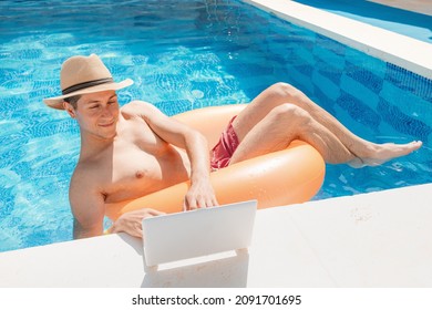 Relaxed Man Floating With Inflatable Circle In Swimming Pool And Surfing The Internet Websites At Laptop Or Notebook Pc. Leisure Weekend And Remote Freelance Work