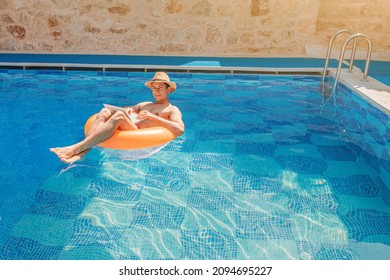 Relaxed Man Floating With Inflatable Circle In Swimming Pool And Surfing The Internet Websites At Laptop Or Notebook Pc. Leisure Weekend And Remote Freelance Work