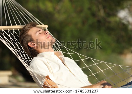Relaxed man sunbathing resting lying on a hammock with eyes closed outdoors in the mountain