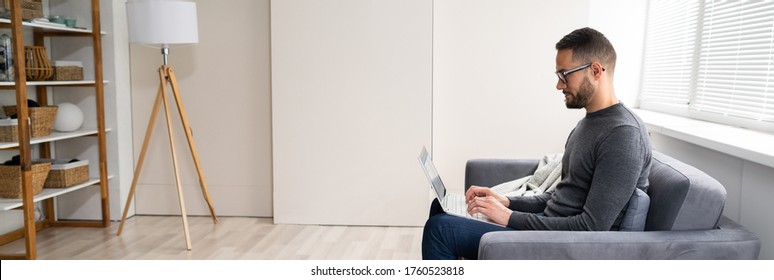 Relaxed Man Using Laptop Computer On Couch At Home