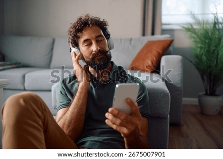 Relaxed man using smart phone while listening music with eyes closed at home. 