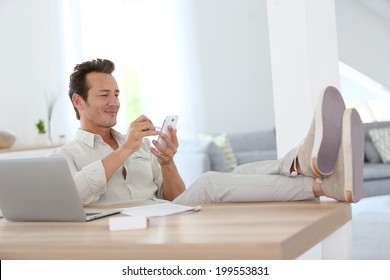 Relaxter Mann, der von zu Hause aus arbeitet und Smartphone verwendet