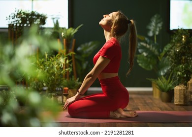 relaxed modern woman in red fitness clothes at modern green home meditating.