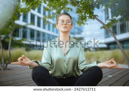 relaxed modern woman worker near office building in green blouse and eyeglasses meditating.