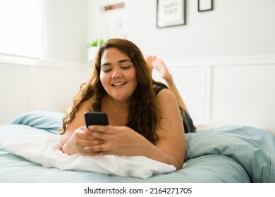 Relaxed obese woman in bed texting on her smartphone and laughing while scrolling social media  - Powered by Shutterstock