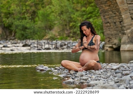 Relaxed pregnant woman in the nature, enjoying a beautiful spot on a river shore.