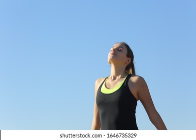 Relaxed runner woman breathing fresh air outdoors with the blue sky in the background
