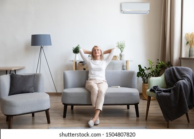 Relaxed satisfied older woman sitting leaning back on couch in air conditioner room, happy peaceful mature female with hands behind head resting on sofa at home, enjoying fresh air, breathing