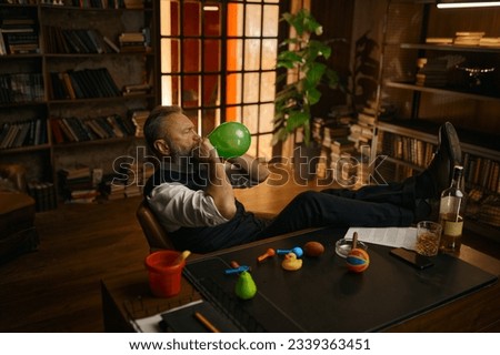 Relaxed senior businessman blowing up balloon while sitting at home office Foto stock © 